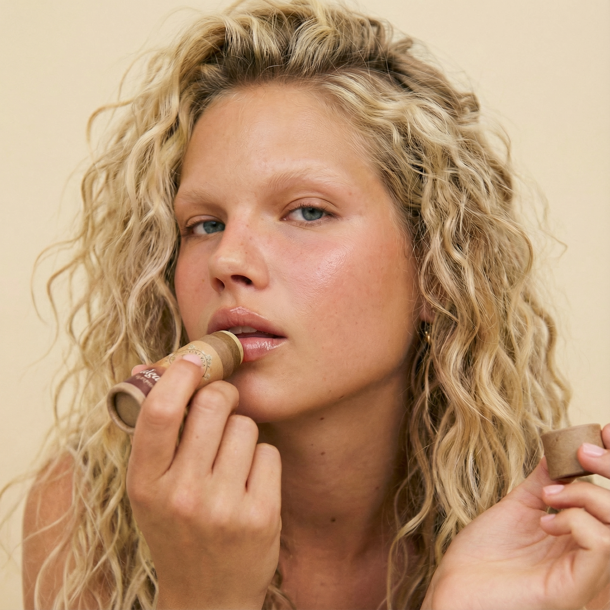 Person applying Talga Kiss tallow lip balm, holding the cap in their other hand.