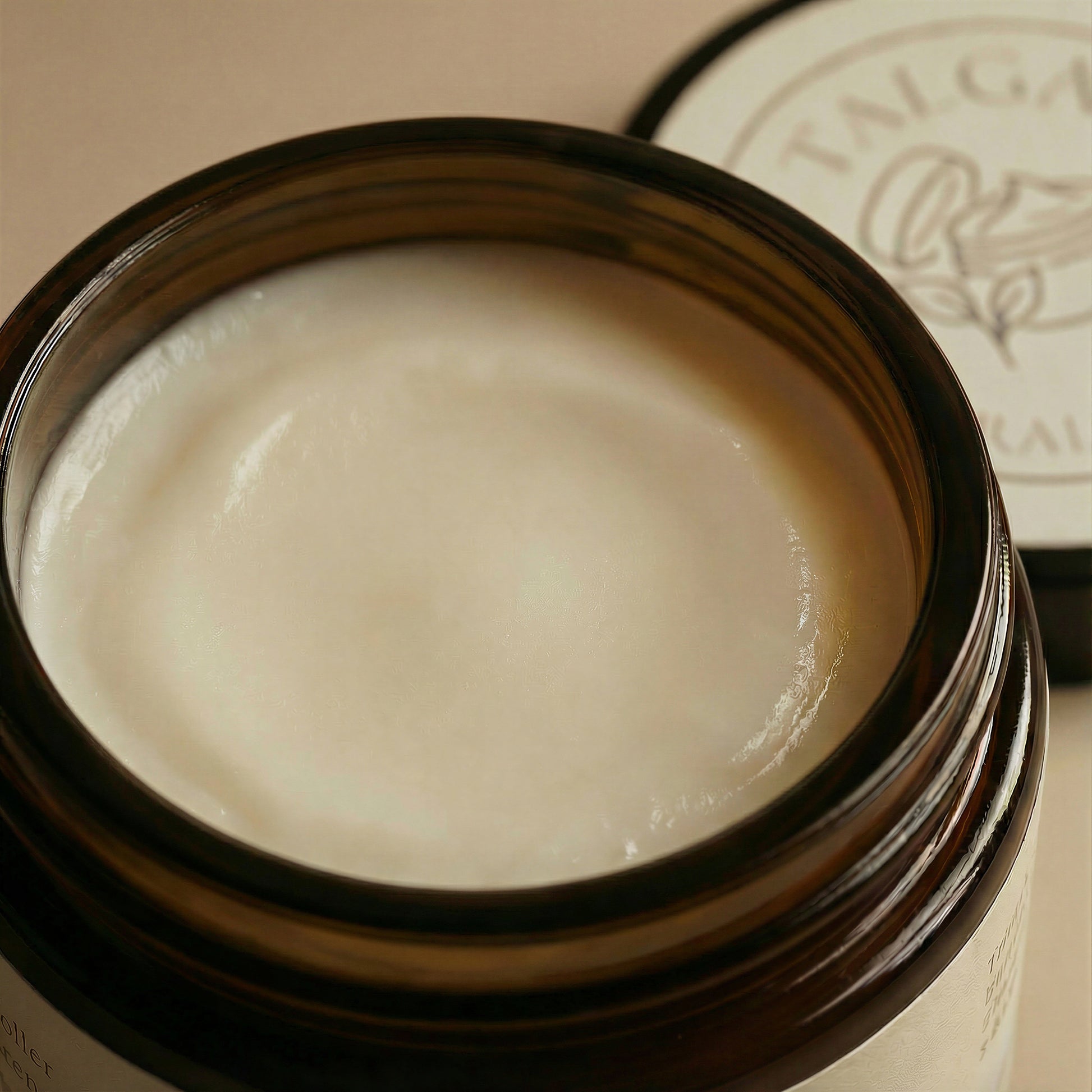 Close-up of Talga Light cream texture in an open amber glass jar, with the lid blurred behind.